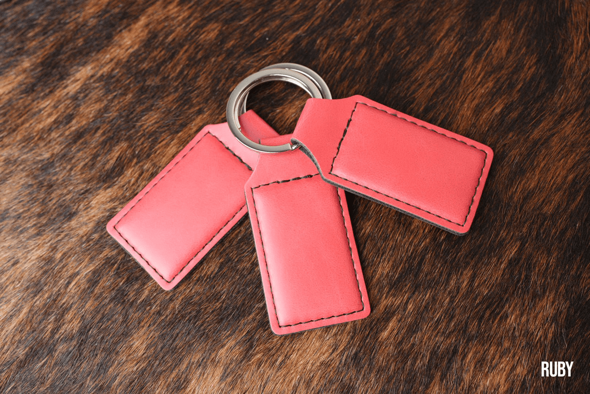 Three Ruby coral red Premium Leatherette keychains fanned out on a split ring, showing the blank engraving panel.