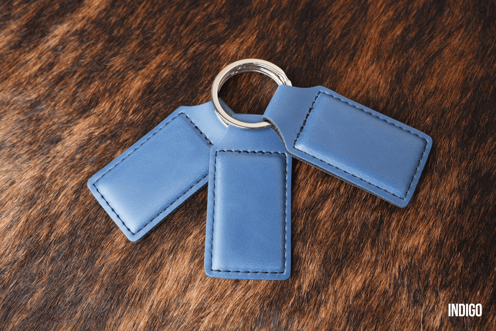 Three Indigo blue Premium Leatherette keychains fanned out on a split ring, showing the blank engraving panel.
