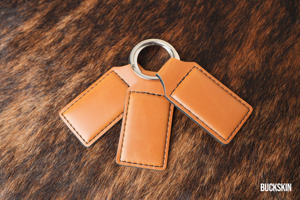 Three Buckskin tan Premium Leatherette keychains fanned out on a split ring, showing the blank engraving panel.