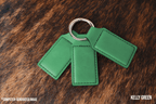 Three Kelly Green Premium Leatherette keychains fanned out on a split ring, showing the blank engraving panel.