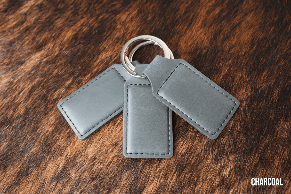 Three Charcoal grey Premium Leatherette keychains fanned out on a split ring, showing the blank engraving panel.