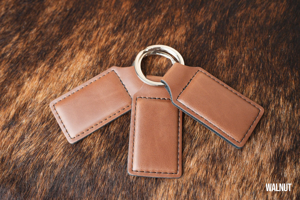 Three Walnut brown Premium Leatherette keychains fanned out on a split ring, showing the blank engraving panel.