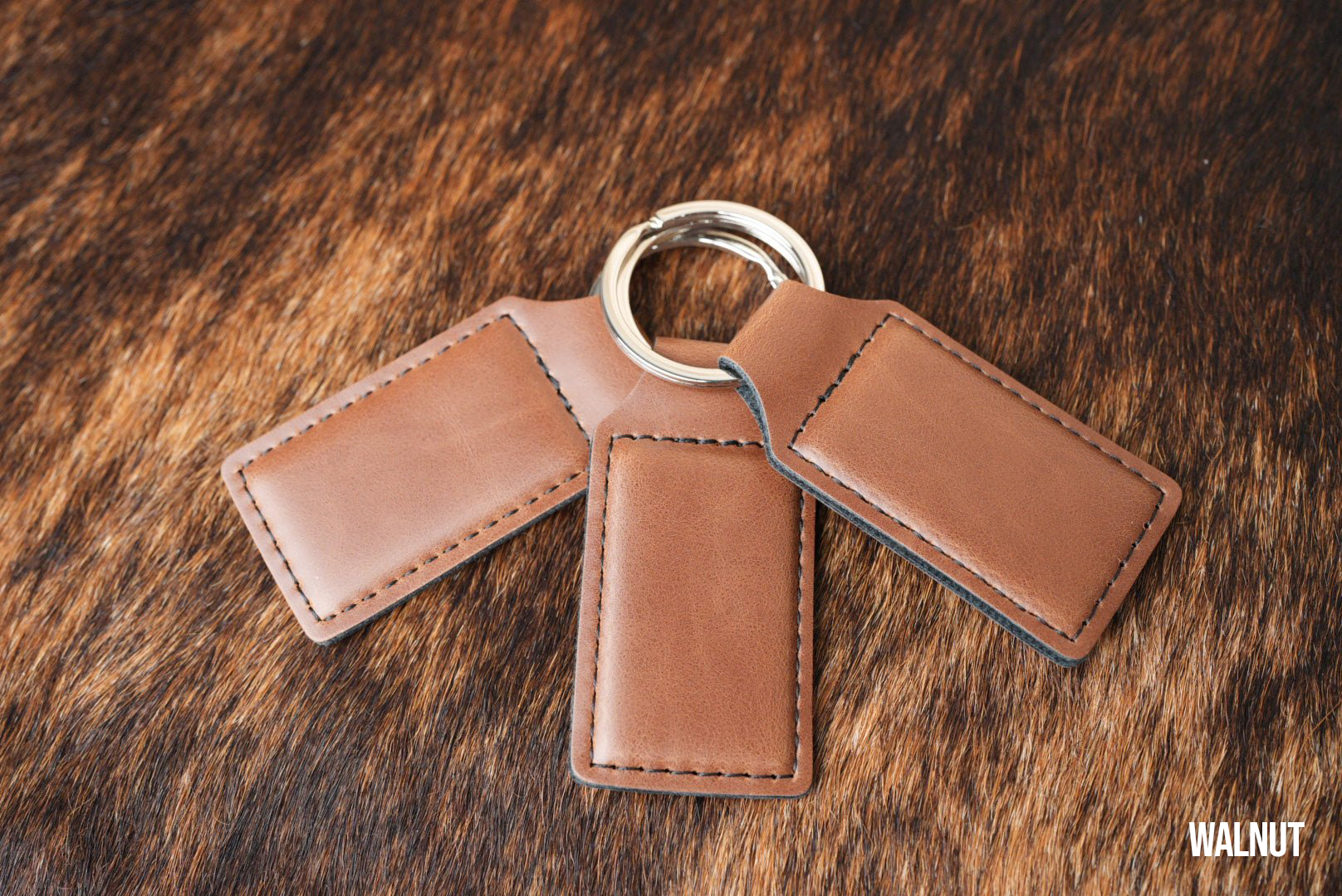 Three Walnut brown Premium Leatherette keychains fanned out on a split ring, showing the blank engraving panel.