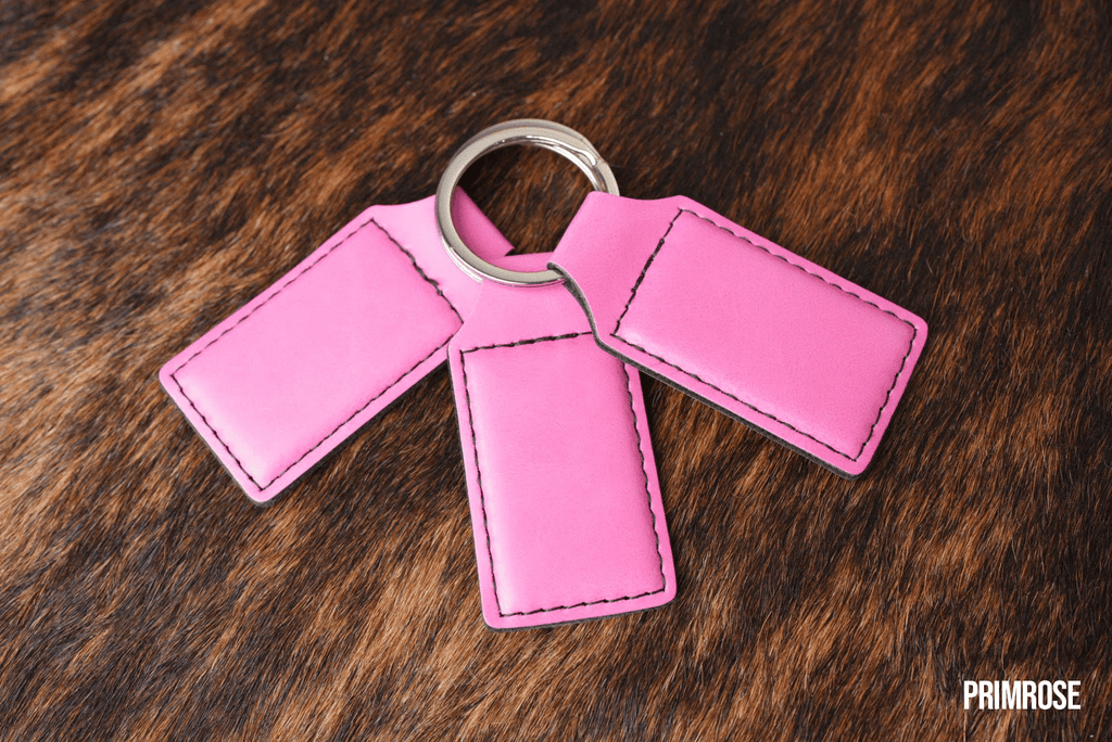 Three Primrose pink Premium Leatherette keychains fanned out on a split ring, showing the blank engraving panel.