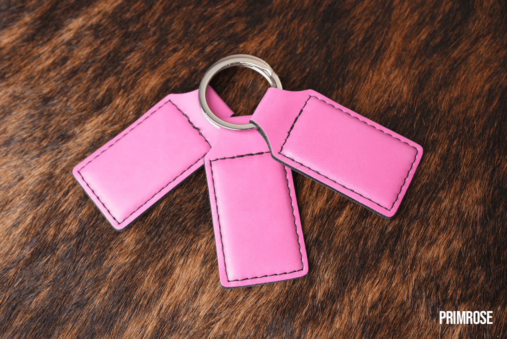 Three Primrose pink Premium Leatherette keychains fanned out on a split ring, showing the blank engraving panel.