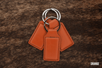 Three burnt orange Premium Leatherette keychains fanned out on a split ring, showing the blank engraving panel.