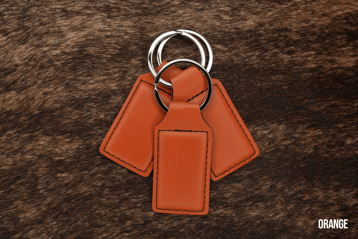 Three burnt orange Premium Leatherette keychains fanned out on a split ring, showing the blank engraving panel.