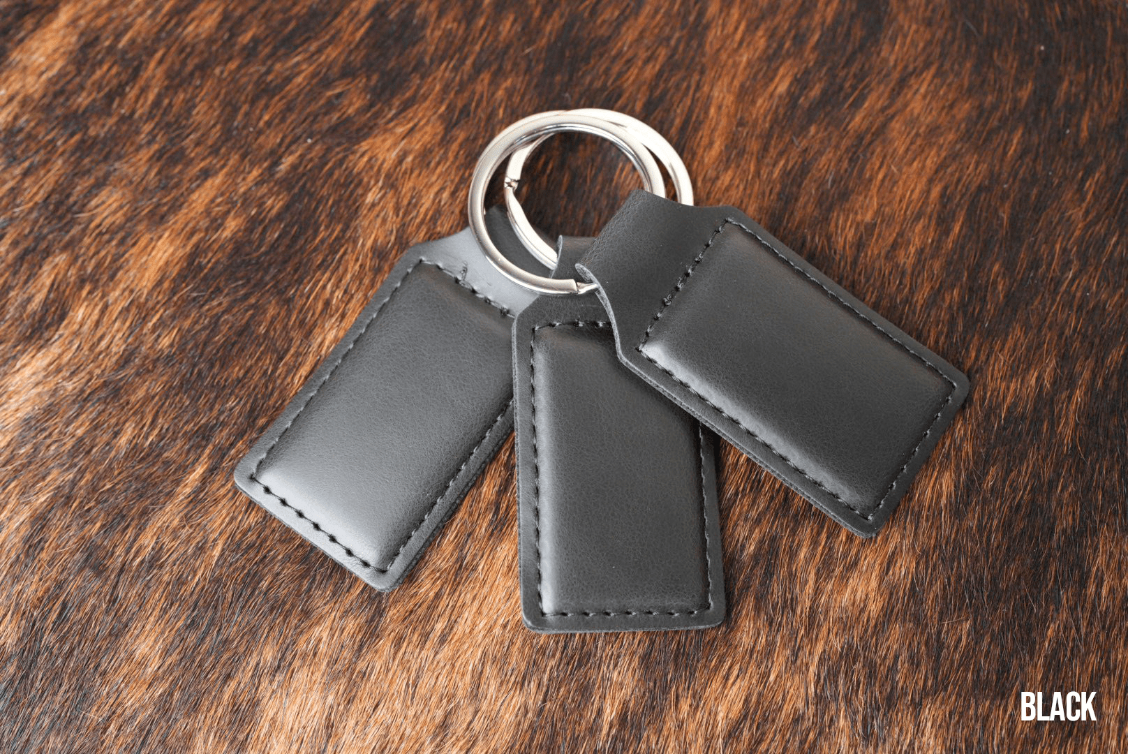 Three Black Premium Leatherette keychains fanned out on a split ring, showing the blank engraving panel.