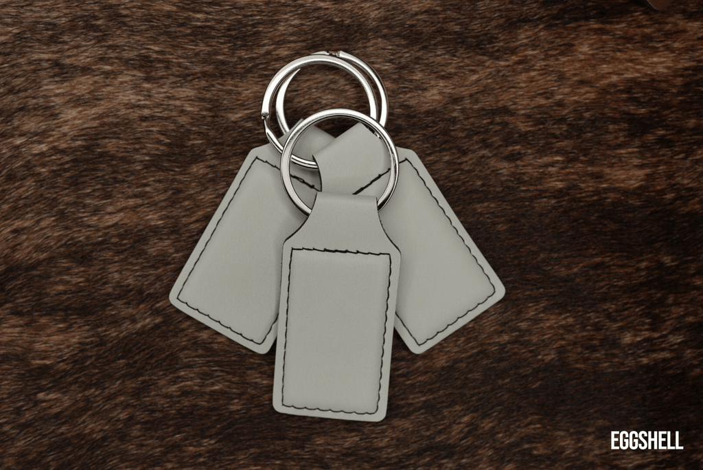 Three Eggshell pale cream Premium Leatherette keychains fanned out on a split ring, showing the blank engraving panel.