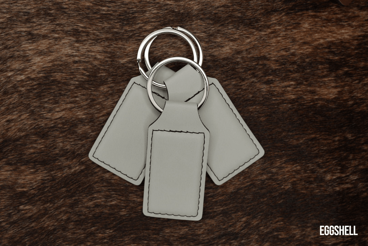 Three Eggshell pale cream Premium Leatherette keychains fanned out on a split ring, showing the blank engraving panel.