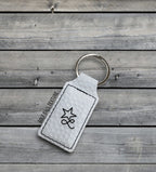 A white golf ball texture Premium Leatherette keychain with a split ring, lying on weathered grey wood, laser engraved with a sample design.