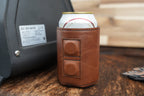 A brown Premium Leatherette magnetic can coozie holding a can, stuck to the side of a metal machine to show the built-in magnets in use