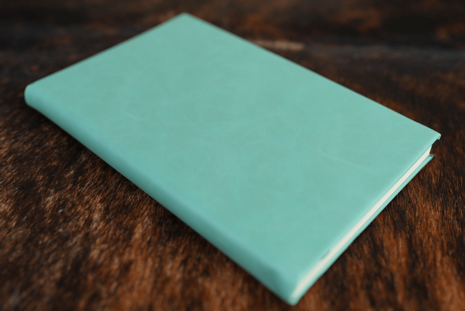 Seafoam Green Premium Leatherette journal cover, shown closed on a cowhide surface
