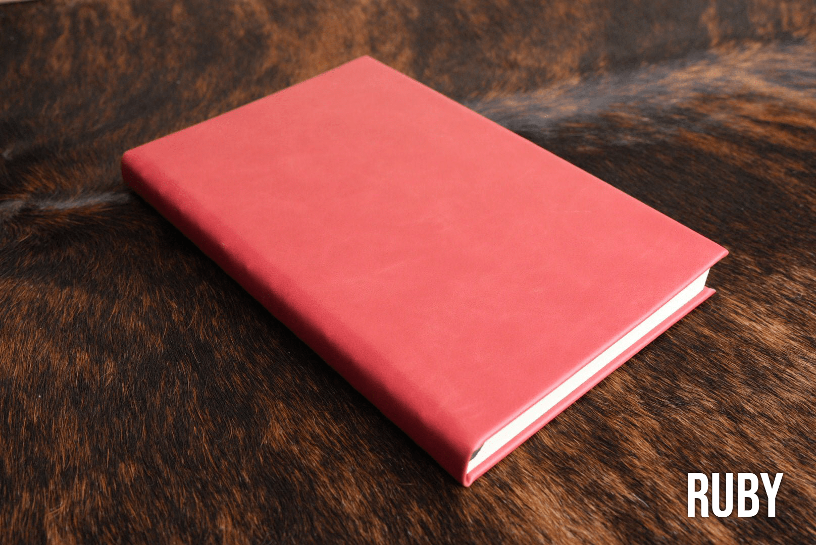 Ruby red Premium Leatherette journal cover, shown closed on a cowhide surface