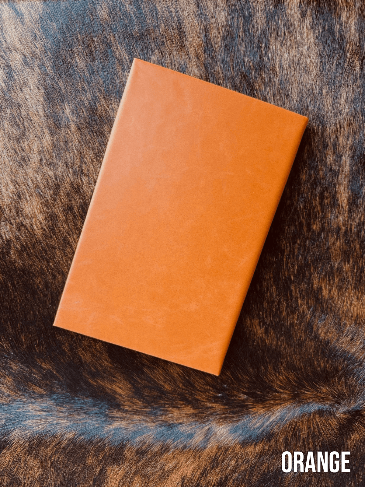 Orange Premium Leatherette journal cover, shown closed on a cowhide surface