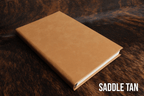 Saddle Tan Premium Leatherette journal cover, shown closed on a cowhide surface