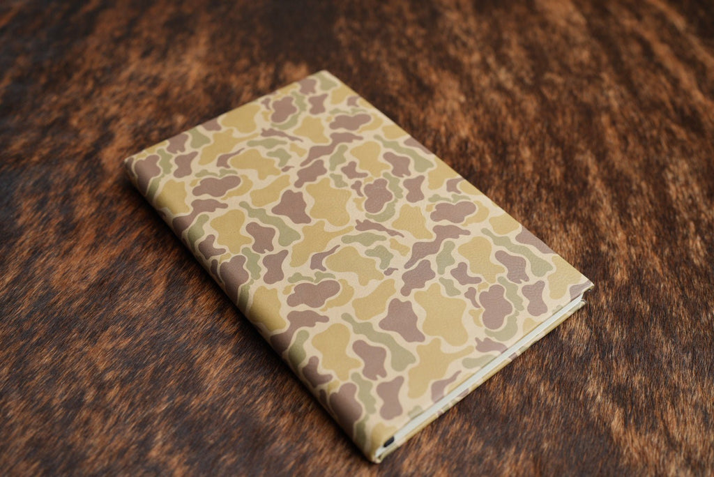 Duck Camo Premium Leatherette journal cover in yellow tan and brown, shown closed on a cowhide surface