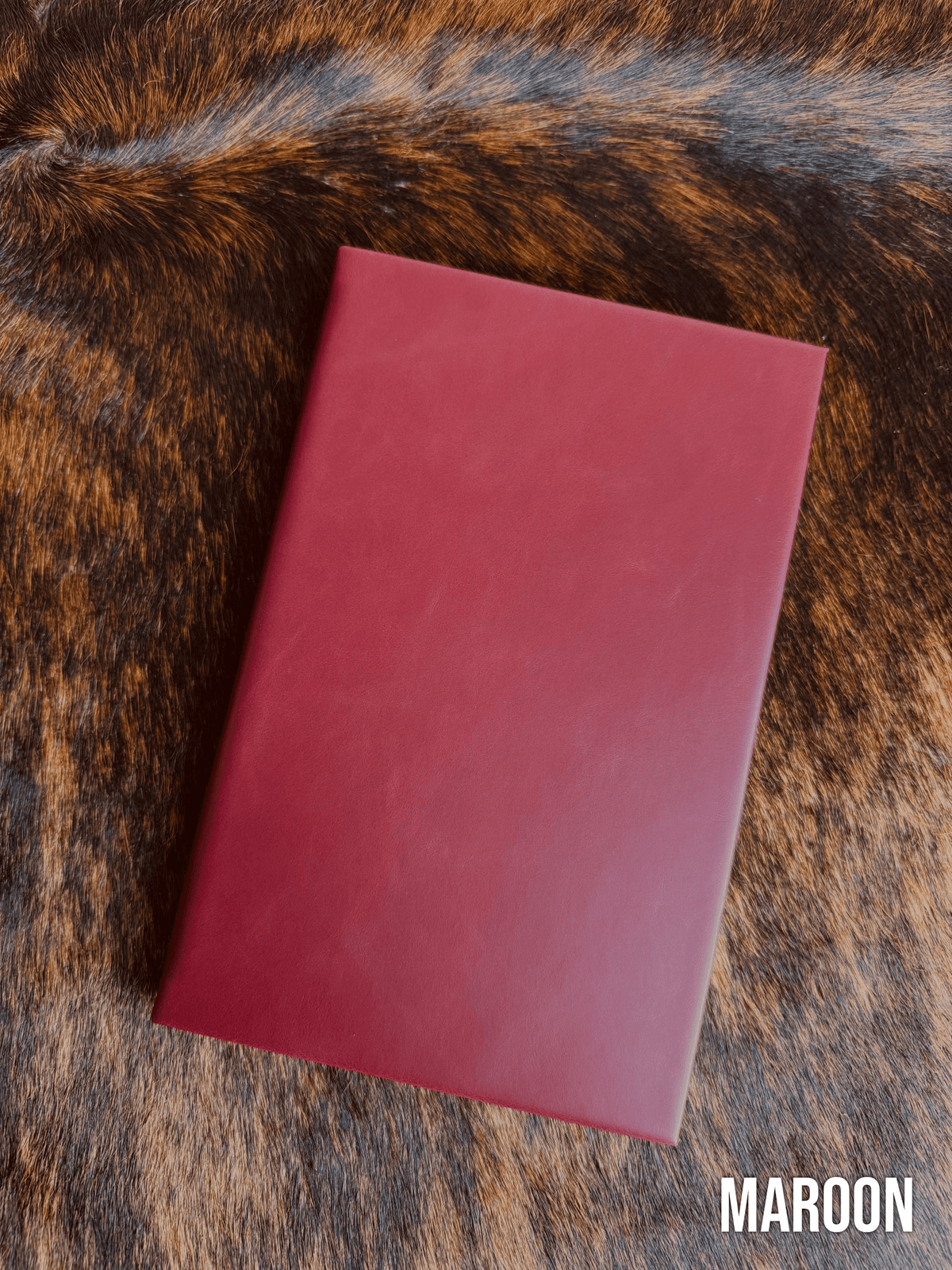Maroon Premium Leatherette journal cover, shown closed on a cowhide surface