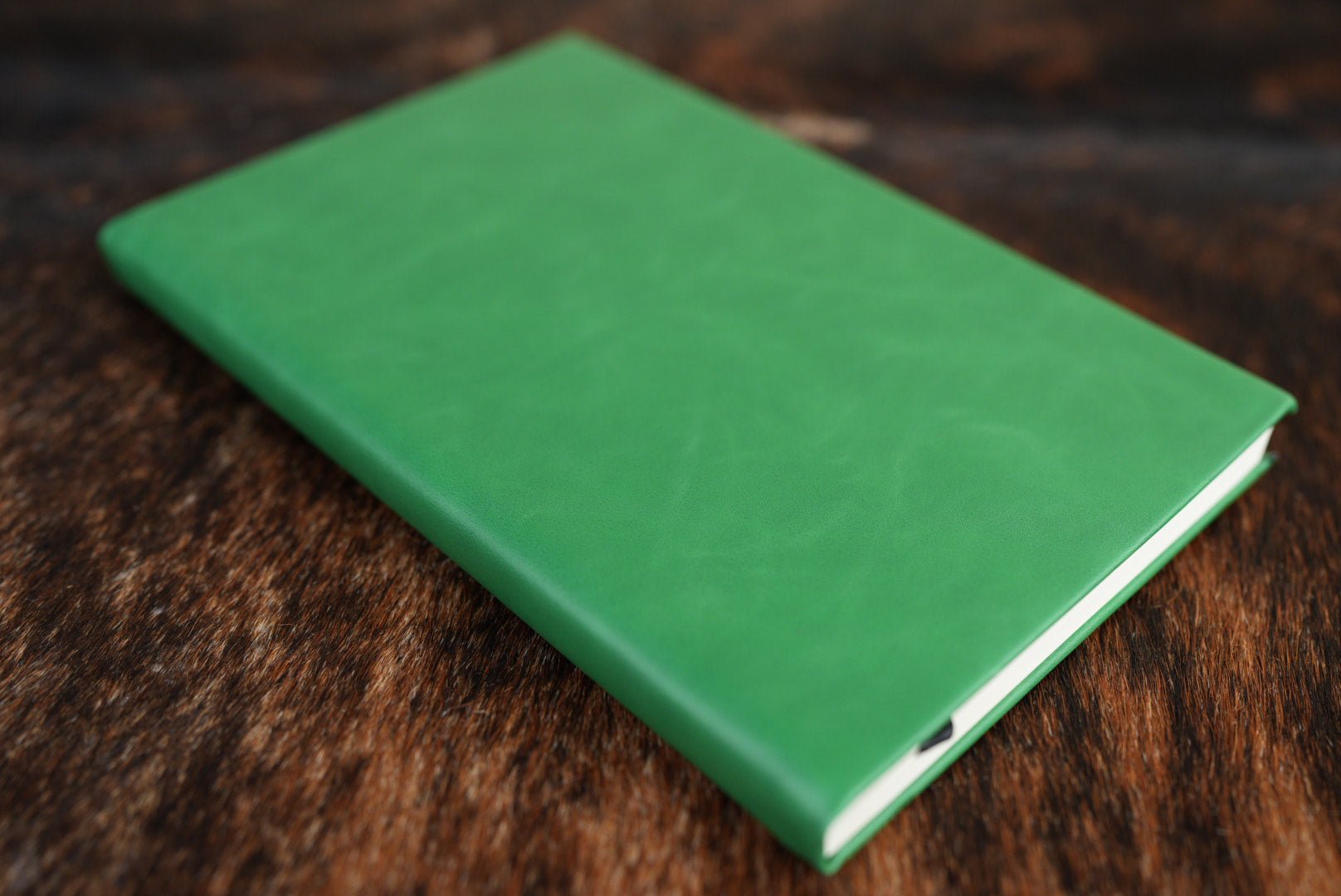 Kelly Green Premium Leatherette journal cover, shown closed on a cowhide surface