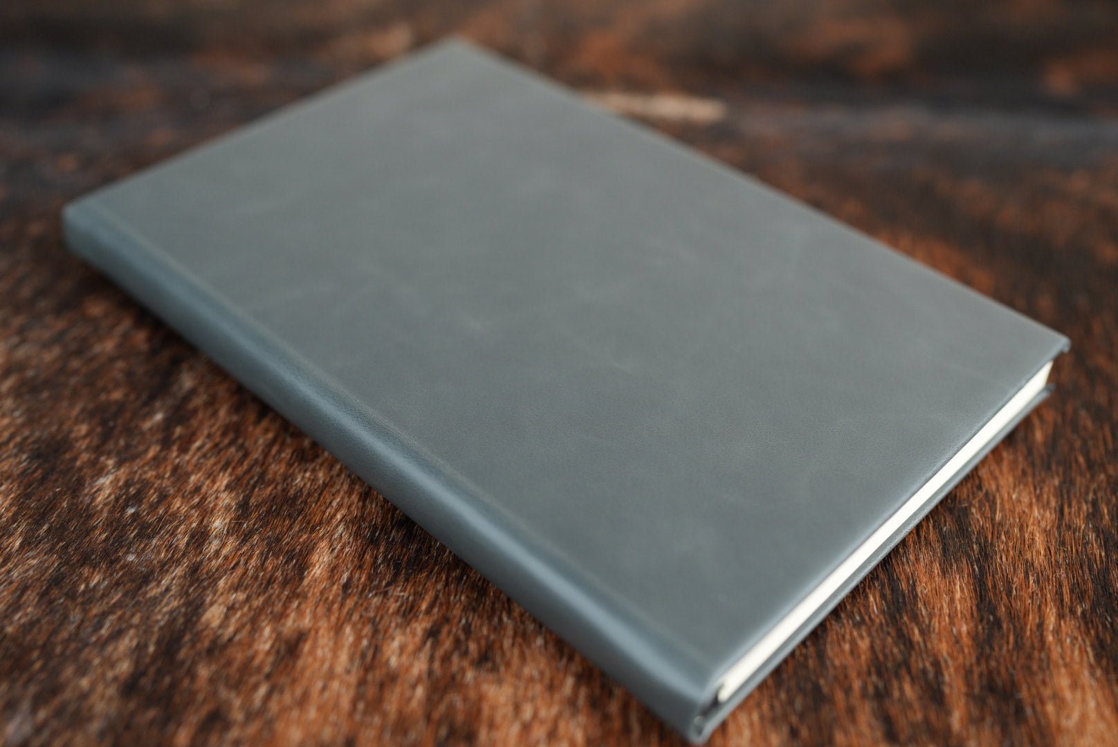 Charcoal gray Premium Leatherette journal cover, shown closed on a cowhide surface