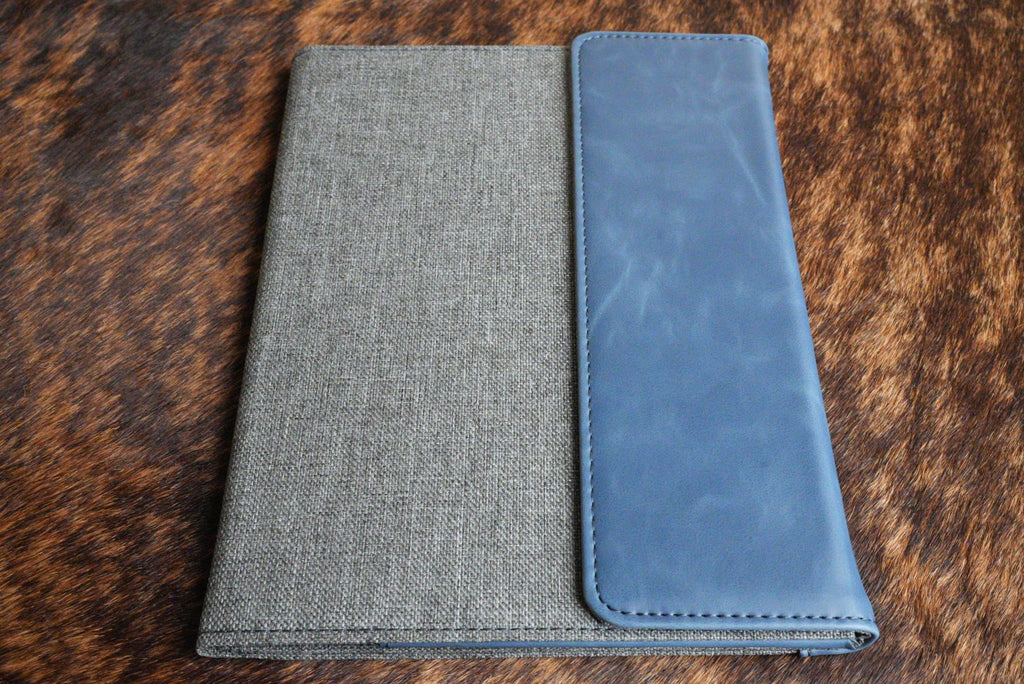 Indigo blue Premium Leatherette padfolio, shown closed on a cowhide surface