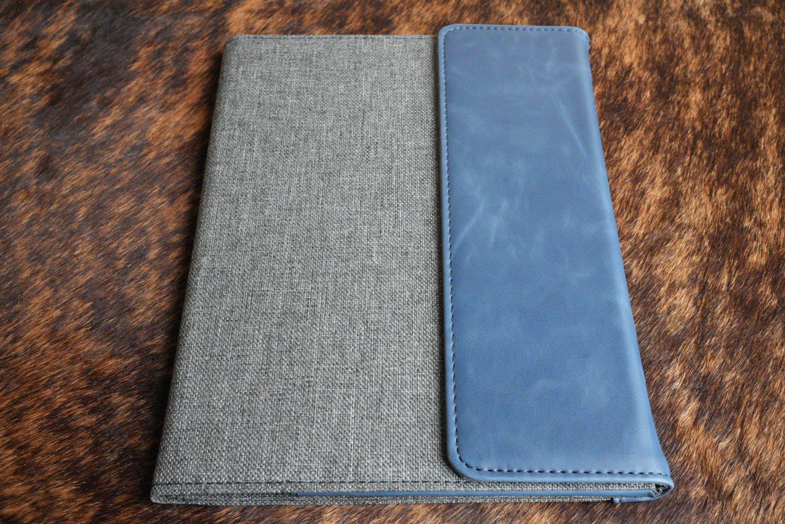 Indigo blue Premium Leatherette padfolio, shown closed on a cowhide surface