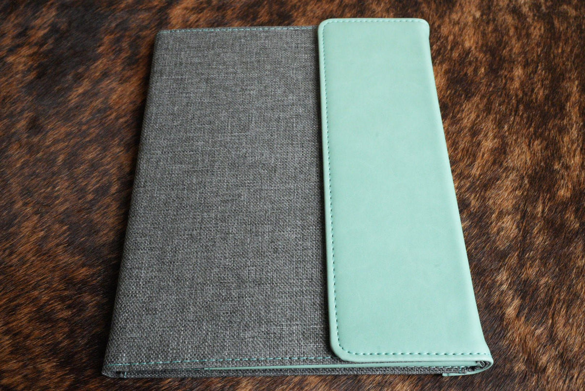 Seafoam Green Premium Leatherette padfolio, shown closed on a cowhide surface