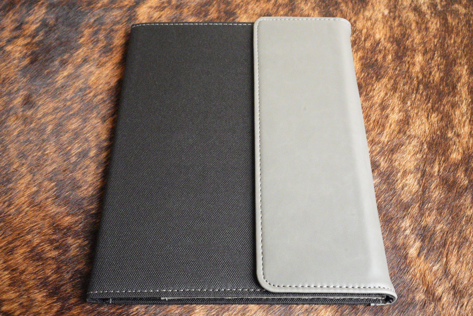 Flint gray Premium Leatherette padfolio that engraves to black, shown closed on a cowhide surface