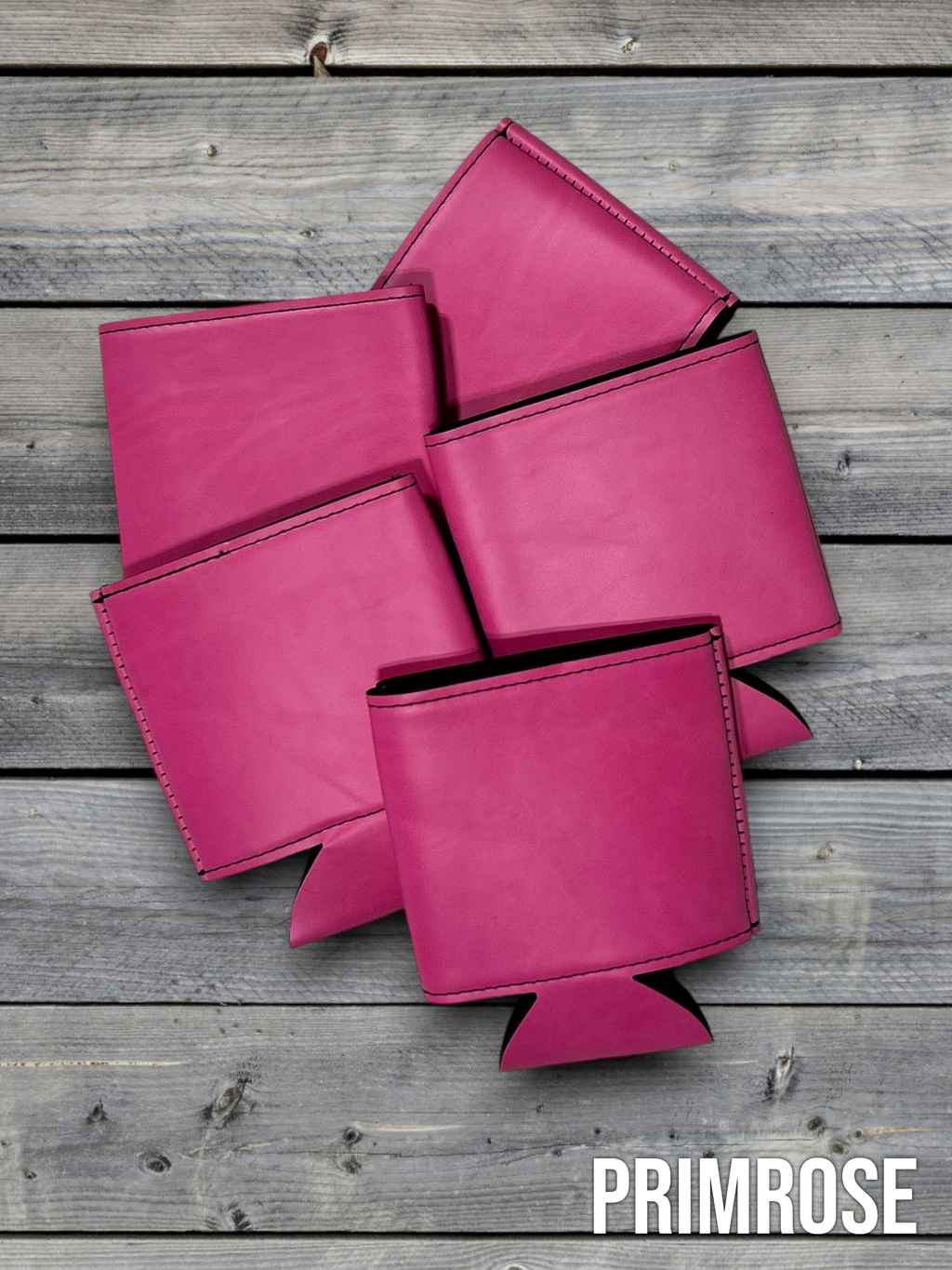 Several Primrose pink Premium Leatherette can coolers laid flat on weathered wood, shown collapsed.