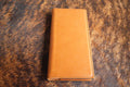 Buckskin tan Premium Leatherette tally book, shown closed on a cowhide surface