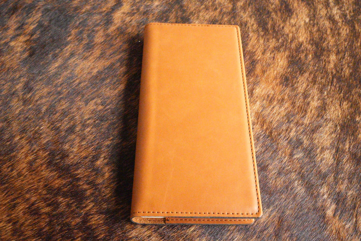 Buckskin tan Premium Leatherette tally book, shown closed on a cowhide surface