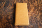 Saddle Tan Premium Leatherette tally book, shown closed on a cowhide surface