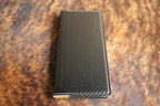 Black carbon fiber Premium Leatherette tally book that engraves to silver, shown closed on a cowhide surface
