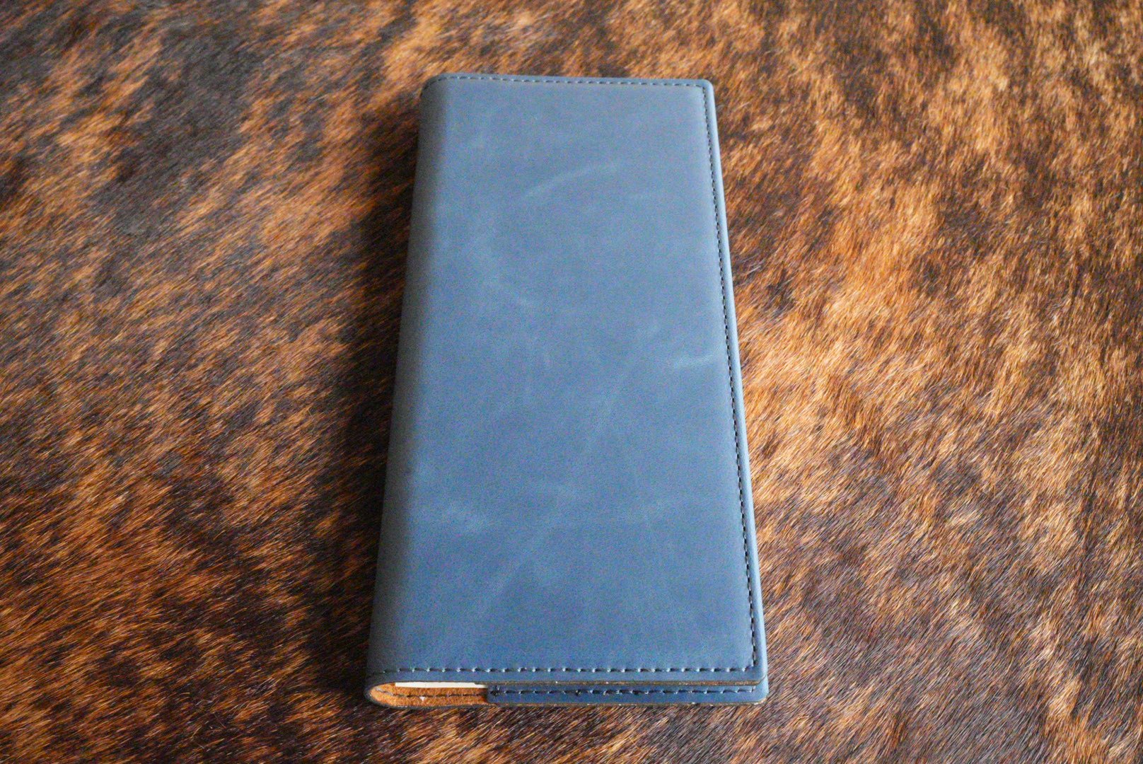 Indigo blue Premium Leatherette tally book, shown closed on a cowhide surface