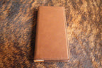 Walnut brown Premium Leatherette tally book, shown closed on a cowhide surface