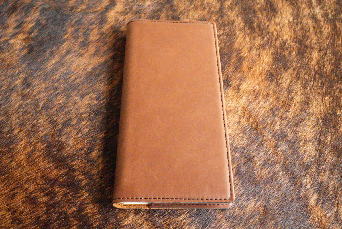 Walnut brown Premium Leatherette tally book, shown closed on a cowhide surface