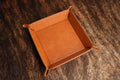 Heritage Rawhide leatherette valet tray with snap corners, shown from above on a cowhide surface