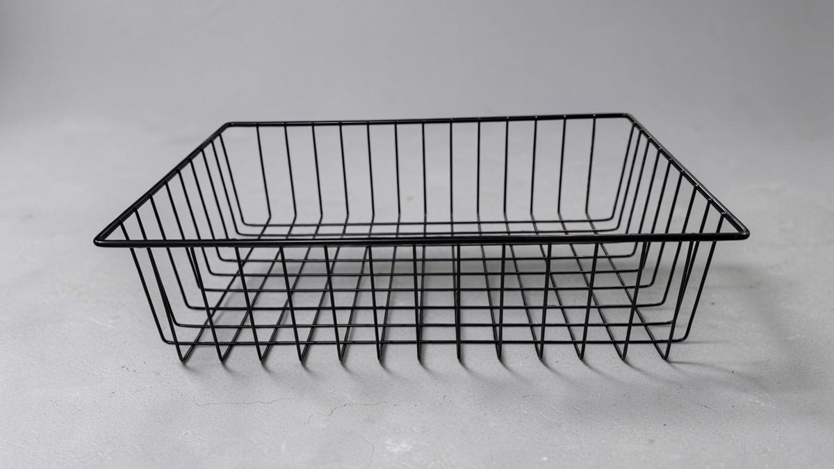 Black wire gift basket, a rectangular open-top frame of welded wire with flared corner legs, on a light grey surface.